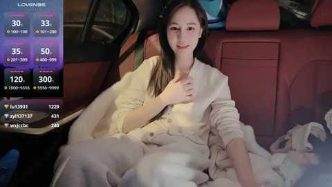 Media: Video of a young East Asian woman in a white robe, seated comfortably in a red leather car interior, surrounded by a dimly lit, modern setting.