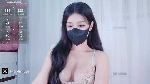 Media: A video of an East Asian woman with long black hair, wearing a black mask and a lacy beige bra, standing in front of a digital clock displaying 11:22.