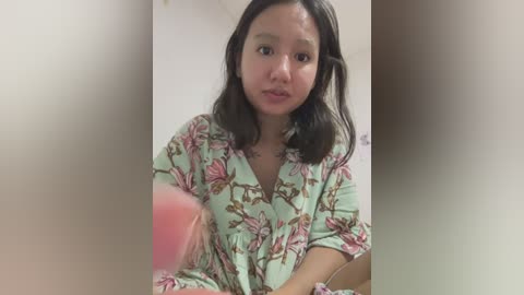 Media: Video of an Asian woman with shoulder-length black hair, wearing a floral-patterned dress, looking curious and slightly distressed, blurred background.