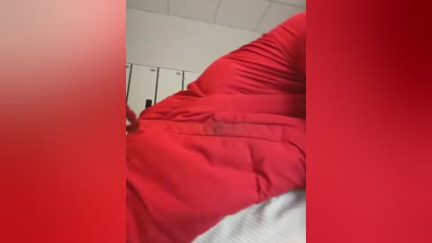 Media: A video of a person in a red shirt, lying on a bed with white sheets, in a room with white walls and a white ceiling.