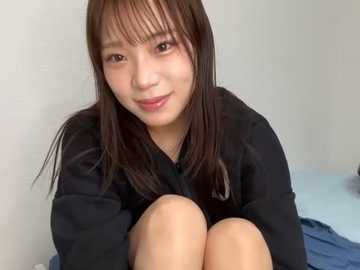 Media: Video of a young Asian woman with straight, dark brown hair and fair skin, wearing a black hoodie, sitting on a bed with blue sheets, smiling softly.