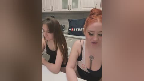 Media: Video of two women, one with long brown hair, the other with red hair in a bun, in a modern kitchen, wearing black tank tops, both looking serious.