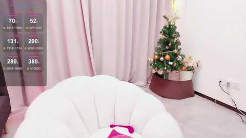 Media: A video of a minimalist room featuring a white, circular bean bag chair in the foreground, a decorated Christmas tree with ornaments, and light pink curtains.