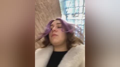 Media: A blurry, grainy video of a young woman with purple hair, wearing a white fur coat, against a brick wall with a blue window. She appears relaxed, eyes closed.