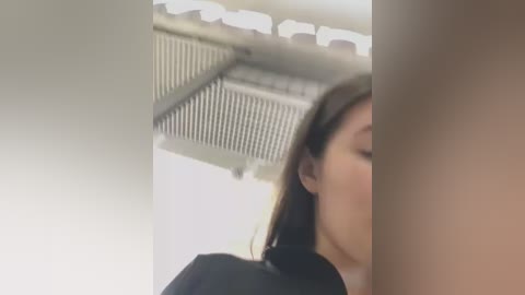 Media: Video of a young woman with long black hair, eyes closed, leaning against a white wall with a ventilation grate, wearing a black top.