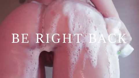 Media: A close-up video of a nude, light-skinned person with soap suds covering their buttocks and lower back. The text \"BE RIGHT BACK\" is superimposed over the image.