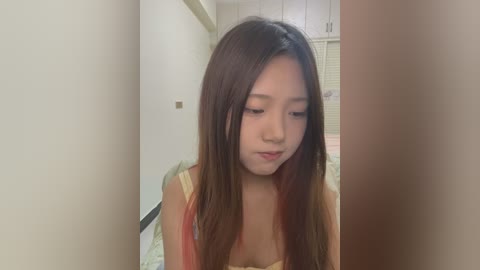 Media: A video of an Asian woman with long, straight brown hair, wearing a sleeveless top, standing in a narrow hallway with white walls and a door in the background.