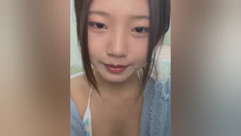 Media: A video of an Asian woman with fair skin, black hair, and a subtle smile, wearing a light blue cardigan and a white top. The background is blurred, focusing attention on her face.