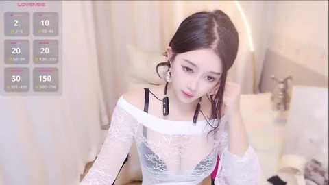 Media: A video of an East Asian woman with long black hair, wearing a white lace dress, in a bedroom. She has a fair complexion, and the room features a bed and a nightstand.