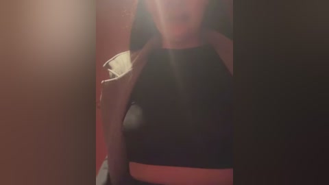 Media: Video of a woman in a black halter top, her face partially obscured, in a dimly lit room.