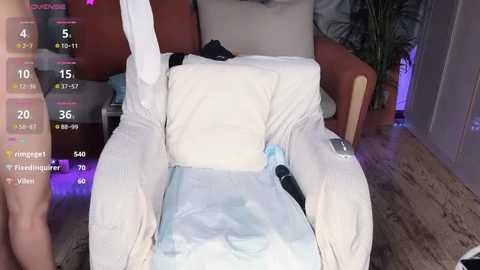 Media: A video of a person reclining in a plush, white armchair, wearing a light blue shirt, with a digital overlay showing vitals and a \"temperature\" of 36.6\u00b0C.