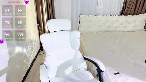 Media: Video of a modern, white leather recliner chair in a minimalist bedroom with beige walls, a tufted headboard, and sheer curtains.