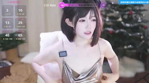 Media: Video of a young Asian woman with short black hair, wearing a silver sequined dress, sitting in a cozy room with a Christmas tree and potted plants.