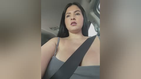 Media: Video of a plus-sized Latina woman with long black hair, wearing a grey tank top, driving in a car with a seatbelt across her chest.