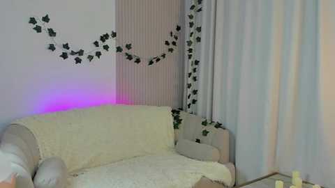 Media: Video of a cozy living room with a cream-colored sofa, white drapes, and a purple LED strip on the wall. Decorative ivy patterns adorn the walls.