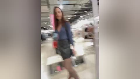 Media: A blurred video shows a woman in a blue blouse and dark skirt walking through a dimly lit car showroom with numerous vehicles in the background.