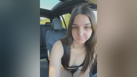 Media: Video of a young woman with long dark hair, fair skin, and small breasts, sitting in a car, wearing a black bra, with blurred background of a vehicle interior.