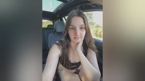 Media: Video of a young Caucasian woman with long brown hair, wearing a black bra, resting her chin on her hand in a car seat.