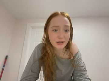 Media: A video of a young Caucasian woman with long, wet, reddish-brown hair, wearing a gray off-shoulder sweater, leaning forward in a room with white walls and a door in the background.