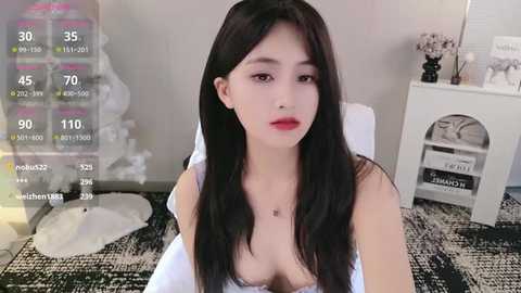 Media: A young East Asian woman with long black hair, fair skin, and red lipstick sits in a modern, minimalist room with white furniture, a grey rug, and a virtual fitness app overlay.