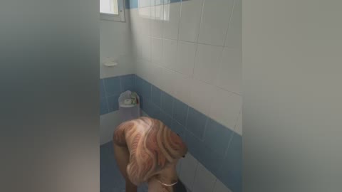 Media: A video of a small, light-skinned child with light brown hair and a round face, peering over a blue and white tiled bathroom sink. The child's back is to the camera.