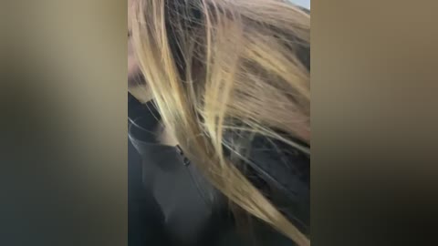 Media: A close-up video of a woman's long, blonde hair, partially obscured by a dark, possibly black, garment, with blurred background.