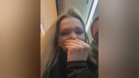 Media: A video shows a young woman with long, messy hair, covering her mouth with one hand, standing in a narrow, dimly lit corridor.