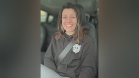 Video of a smiling woman with shoulder-length brown hair wearing a black shirt and seatbelt, seated in a car with a blurred background.