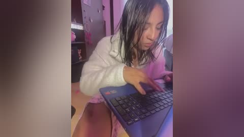 Media: Video of a young Asian woman with wet, dark hair in a white hoodie, typing on a laptop, indoors with dim lighting and pink accents.