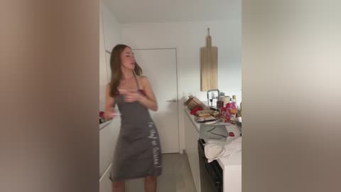 Media: A blurry video shows a woman in a grey apron dancing in a small, messy kitchen with a wooden spoon, amidst cluttered countertops.