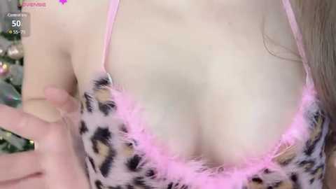 Media: Video of a woman with fair skin wearing a leopard-print bra with pink feather trim, revealing cleavage. Background shows a blurred Christmas tree.