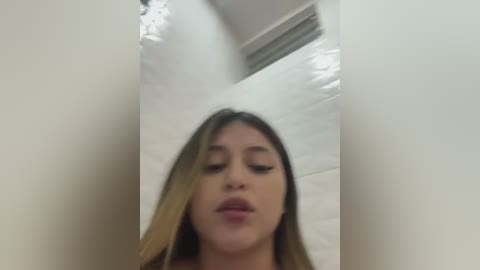 Media: A video of a young woman with long, light brown hair, light skin, and full lips, making a kissy face in a white bathroom with a shower curtain.