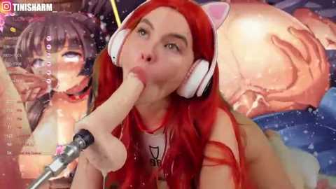 A digital image of a red-haired woman with cat ears, wearing a white top, sucking a large, realistic-looking dildo. Background includes a video overlay of a face with purple hair and a cartoon cat's head.