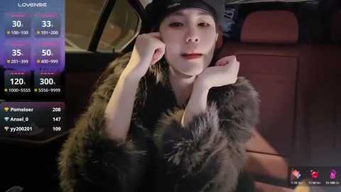 Media: A video of a young Asian woman in a fur coat, sitting in a car at night, wearing a black cap and holding her face.