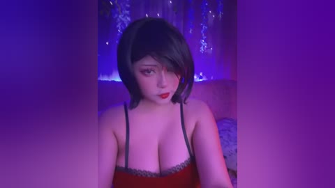 Media: A video of a young woman with short, dark hair, red lipstick, and large breasts, wearing a revealing red lace-trimmed camisole, against a purple-lit, sequined backdrop.