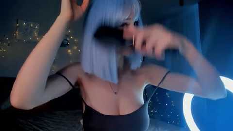 Media: A video of a woman with light skin and short, platinum blonde hair, wearing a black strapless top, with a large, dark, furry object covering her face, in a dimly lit bedroom with a glowing moon and stars on the wall.