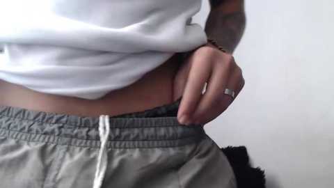 Media: A video of a person wearing a white crop top and gray sweatpants, with a tattooed arm visible, holding the sweatpants' drawstring. The background is plain white.