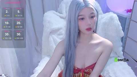 Media: Video of a young East Asian woman with long, platinum blonde hair, fair skin, and red lipstick, wearing a red strapless top, seated on a plush white fur rug.