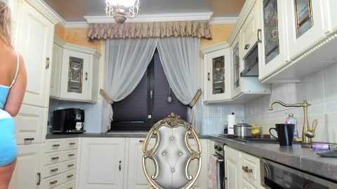 Media: Video of a cozy, vintage-style kitchen with white cabinets, a purple curtain, a black toaster, and a fancy, tufted, gold chair.