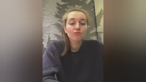 Media: A video of a young woman with fair skin, straight brown hair, and a light blue sweater, making a kissy face in front of a forest-themed wallpaper.