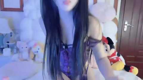 Media: A video of a young Asian woman with long black hair, wearing a purple lace lingerie set, posing in a bedroom with stuffed animals and a Mickey Mouse plush.