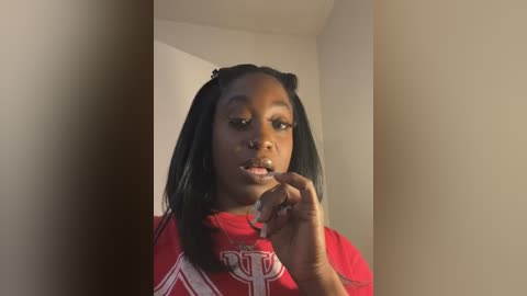 Media: A young Black girl with medium skin tone and straight black hair in two pigtails, wearing a red T-shirt, brushes her teeth in a beige bathroom.