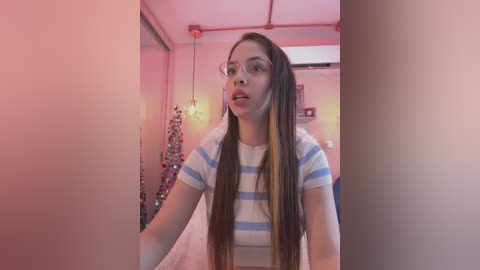 Media: Video of a young woman with long, straight brown hair, wearing a white and blue striped t-shirt, looking surprised with her mouth open. Pinkish lighting, hanging decorations, and a bed in the background.