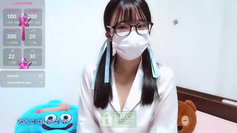 Media: Video of an Asian woman with long black pigtails, wearing a white lab coat, face mask, and glasses, standing indoors.