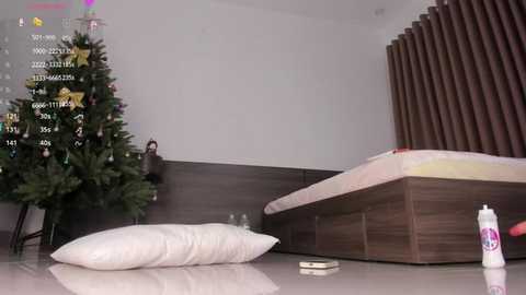 Video of a modern bedroom with a Christmas tree, a bed, and a white pillow on the floor.