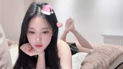 Media: A video of an Asian woman with long black hair, lying on a bed in a cozy, minimally decorated room. She wears a red Santa hat and a heart hairpin. Her expression is serene.