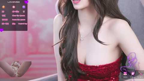 Video of a fair-skinned woman with long, dark brown hair, wearing a strapless red sequined dress, smiling. Background shows blurred pink and white abstract art.