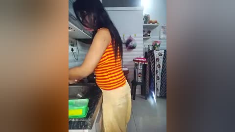 Media: A video shows a woman in a striped orange-and-yellow top, preparing food in a modern kitchen with white cabinets, a green cutting board, and a red stool.