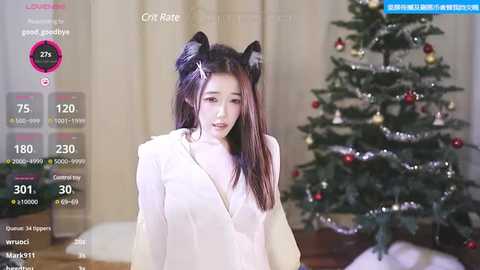 Media: Video of a young East Asian woman with long black hair, wearing a white dress, cat ears, and standing beside a decorated Christmas tree.