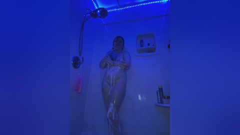 Media: A video of a nude woman with fair skin and long hair showering in a dimly lit bathroom with blue LED lighting. She is standing under a showerhead, with soap suds covering her body.